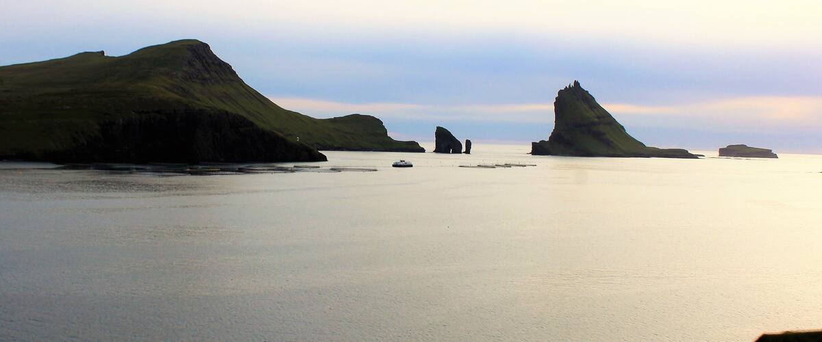 A calm sea with rocky outcrops and a lighthouse in the distance.