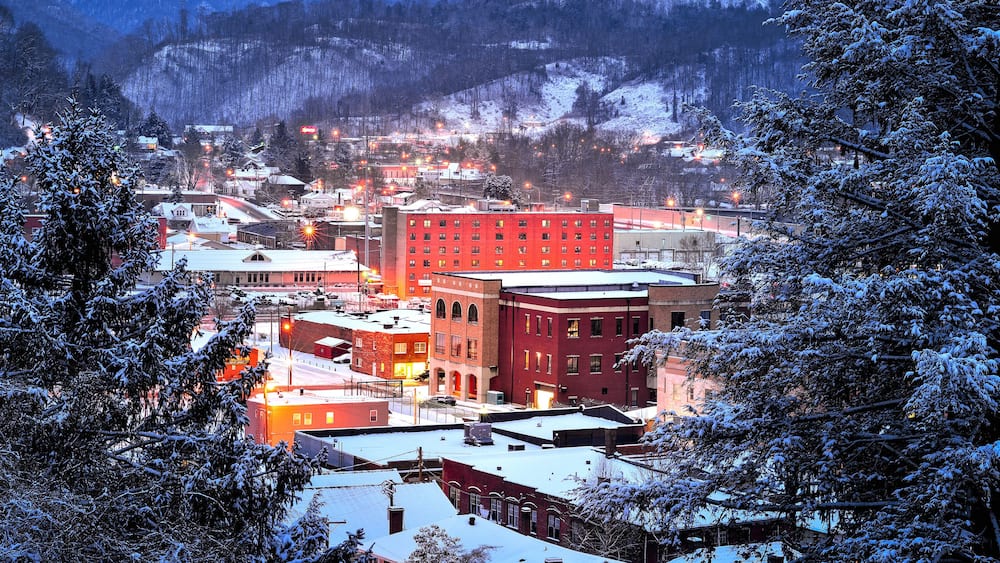 Une ville enneigée au crépuscule, avec des bâtiments illuminés et un imposant bâtiment rouge qui se distingue au centre.