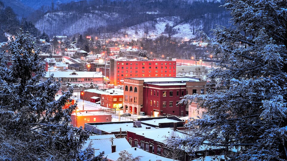 A snow-covered town at dusk with illuminated buildings and a prominent red building in the center.