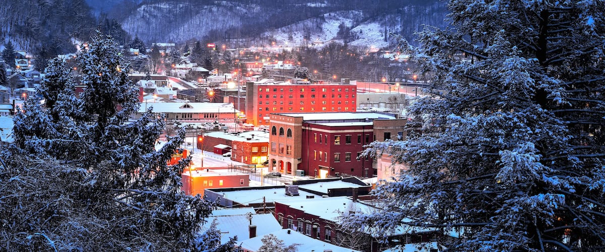 A snow-covered town at dusk with illuminated buildings and a prominent red building in the center.