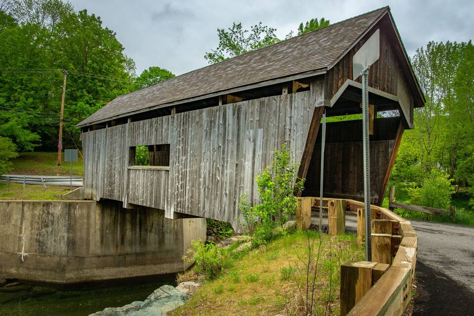 Un puente cubierto de madera con base de concreto, rodeado de follaje y árboles.