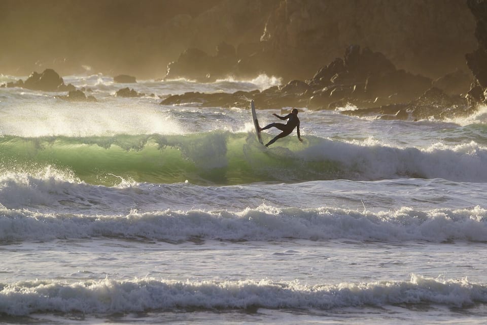 A surfer riding a wave in the ocean with rocky cliffs in the background.