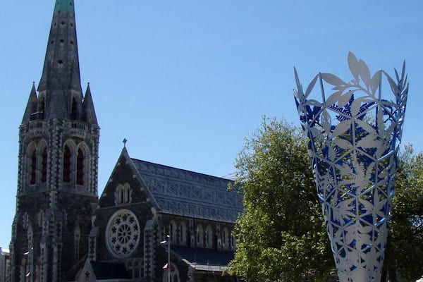 Uma igreja histórica com uma torre alta e uma grande escultura decorativa de metal numa praça pública.