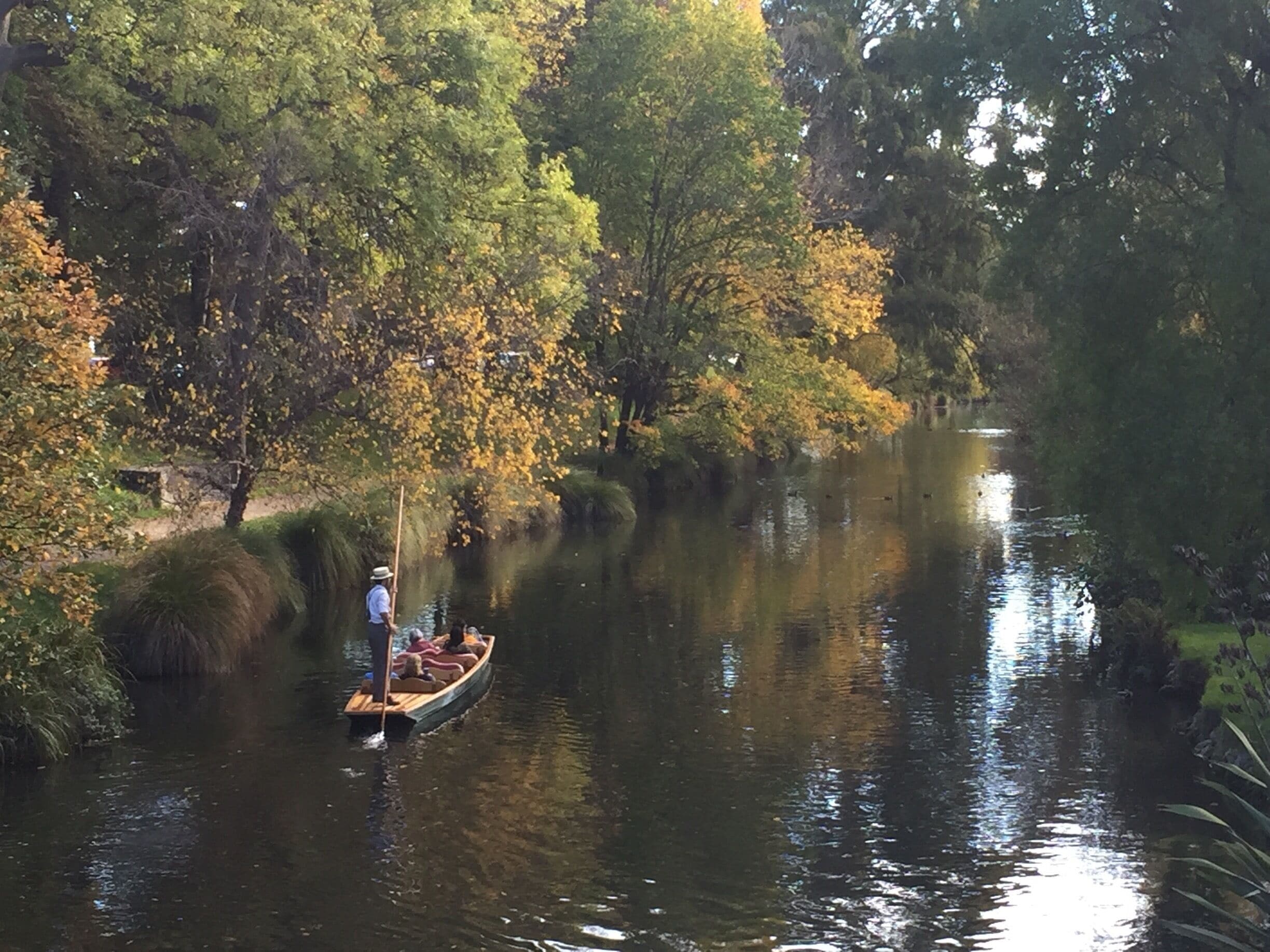 Un río tranquilo con un bote llevando pasajeros, rodeado de árboles con follaje otoñal.