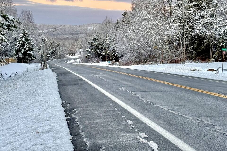A snow-covered road with trees on both sides and a cloudy sky.