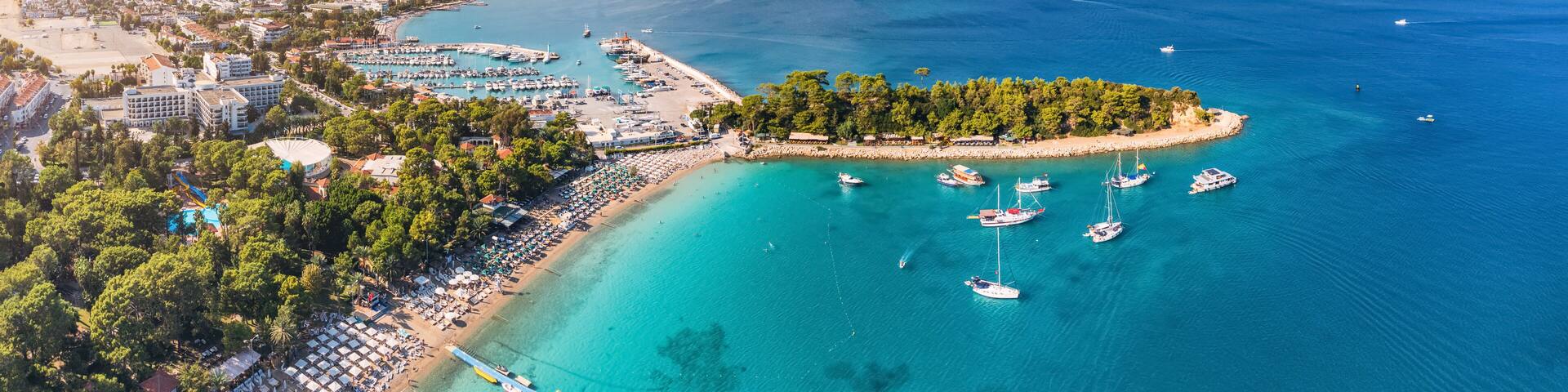 A coastal town with a marina, beach, and mountains in the background.
