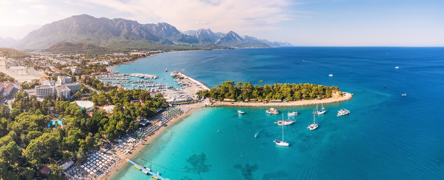 A coastal town with a marina, beach, and mountains in the background.
