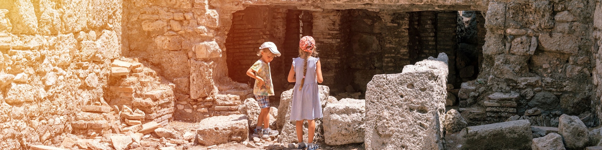 An ancient stone structure with a partially collapsed wall and a large rock in the foreground.