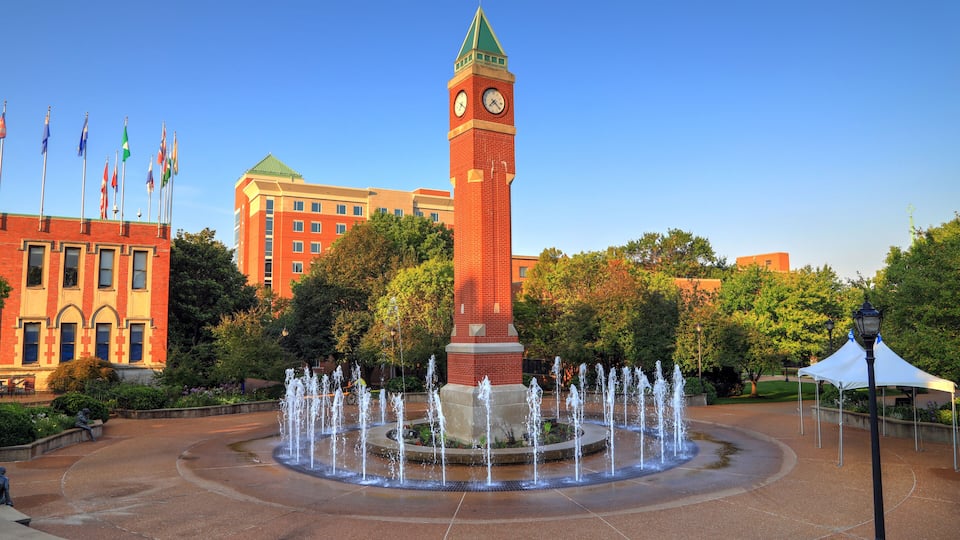 A clock tower, a fountain, and flags in a courtyard.