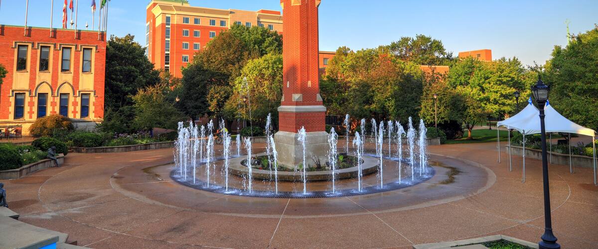 A clock tower, a fountain, and flags in a courtyard.