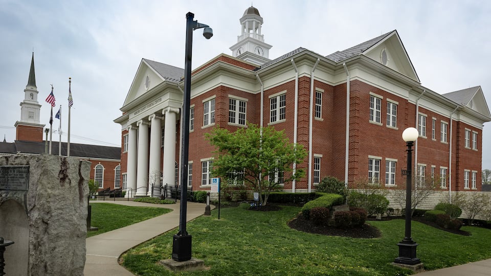A large brick building with a clock tower, surrounded by a well-maintained lawn and street lamps.