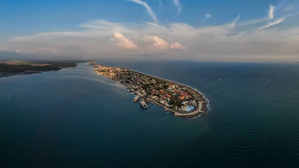 An aerial view of a coastal town with a harbor, surrounded by water and a distant landmass.