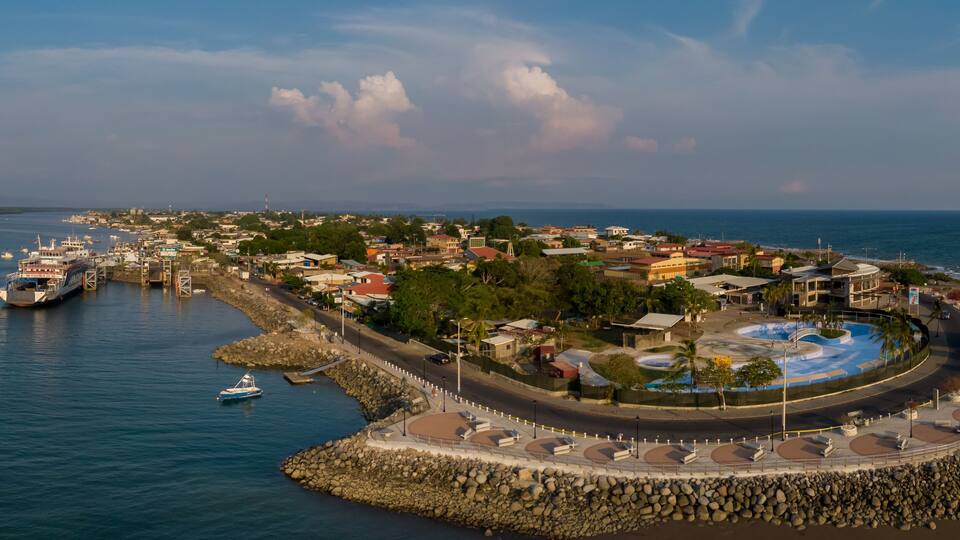 A coastal town with a marina, a lighthouse, and a circular park with a water feature.
