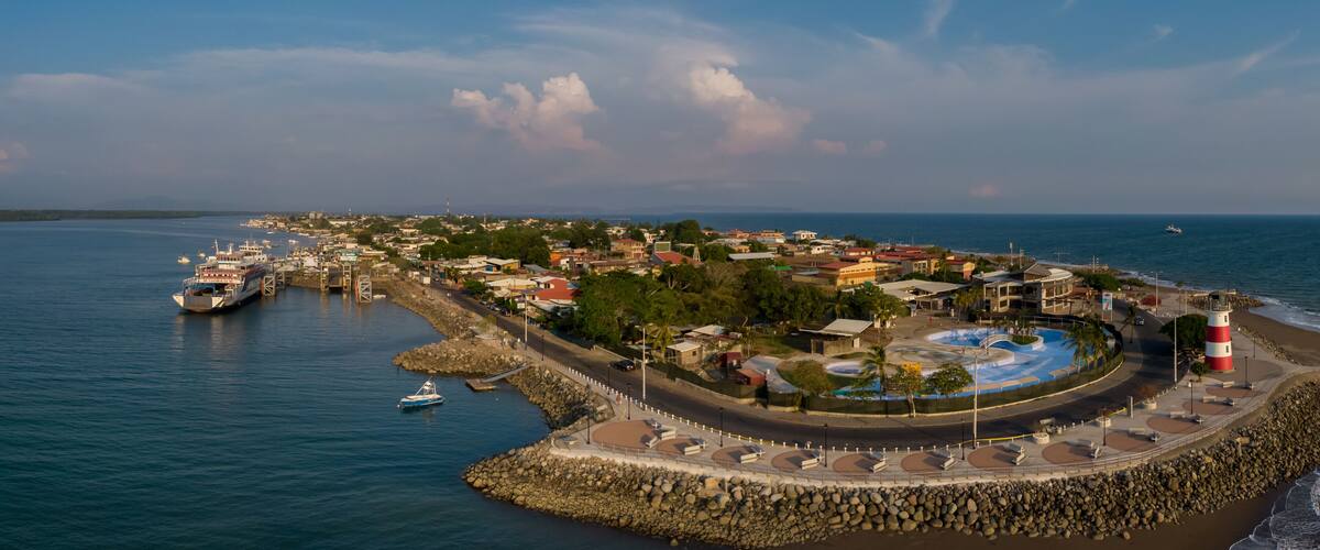 A coastal town with a marina, a lighthouse, and a circular park with a water feature.