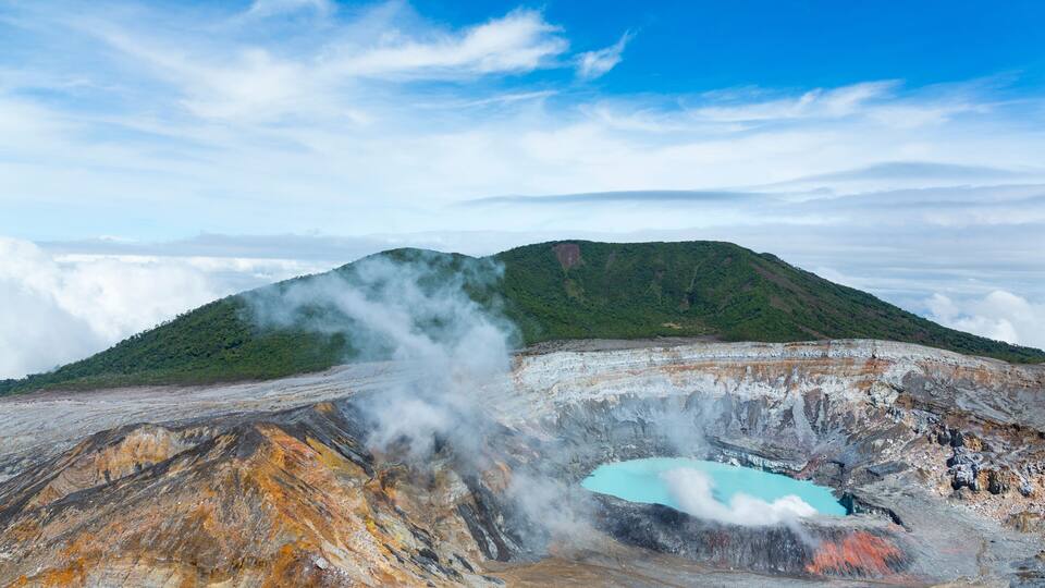 A geothermal area with a blue pool, steam vents, and a green hill in the background.
