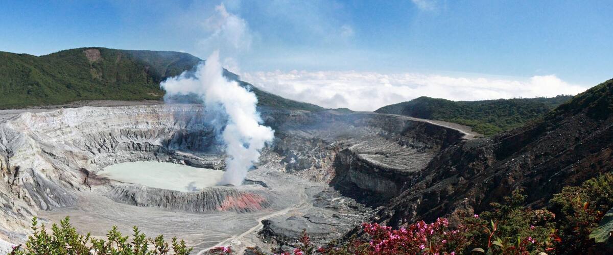 A volcanic crater with a central lake, surrounded by rugged terrain and greenery.