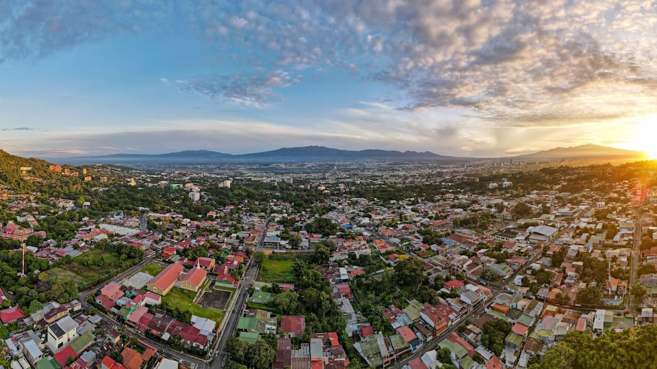 A panoramic view of a city with a mountainous backdrop and a sunset.
