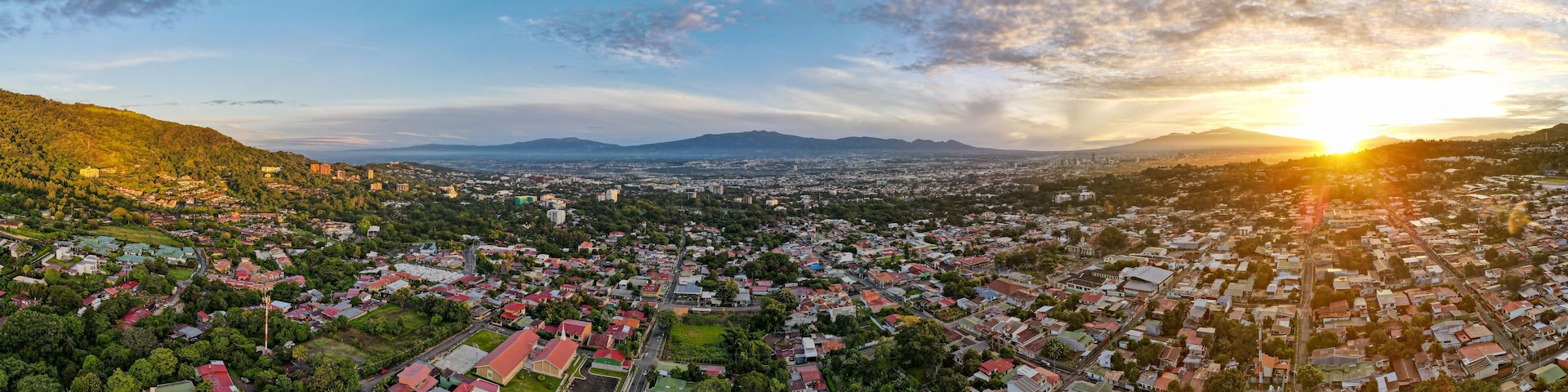 A panoramic view of a city with a mountainous backdrop and a sunset.