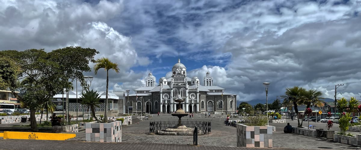 A grand building with domes and arches, surrounded by a plaza with a fountain and palm trees.