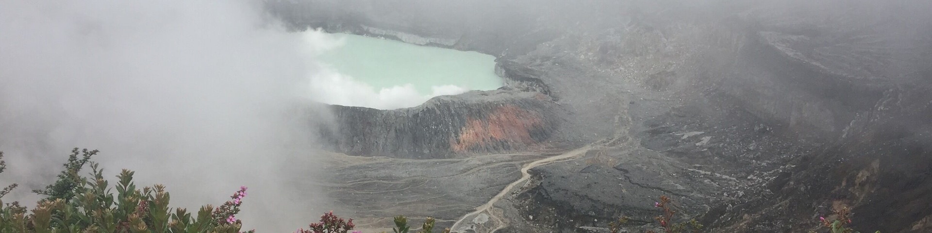 A volcanic landscape with a turquoise lake surrounded by rugged terrain and dense vegetation.