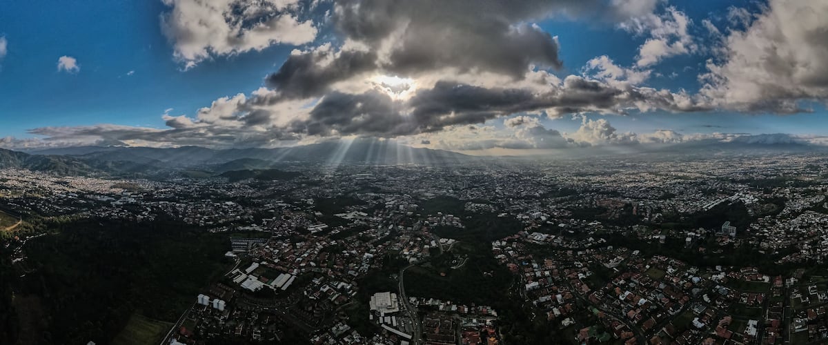 A cityscape with mountains in the background and a cloudy sky.
