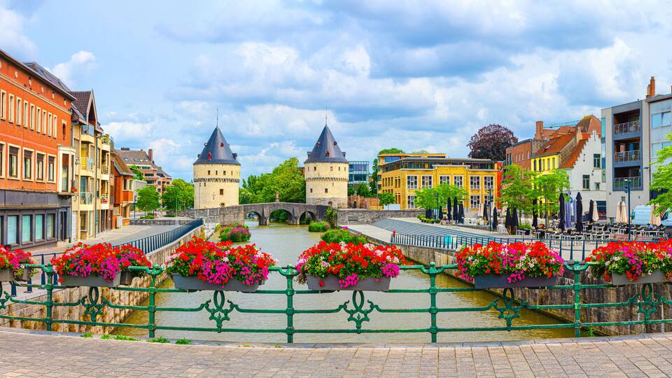 A historic town with a prominent bridge, colorful buildings, and flower-adorned railings.