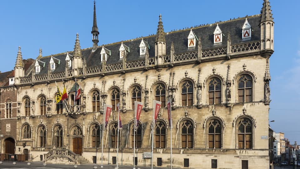 A historic building with Gothic architecture, featuring pointed arches, a tall spire, and multiple flags.