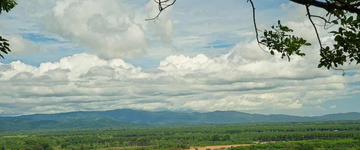 A lush green landscape with a river, distant mountains, and a cloudy sky.
