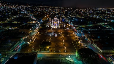 Paisagem urbana noturna com uma catedral imponente no centro, rodeada por ruas e edifícios iluminados.