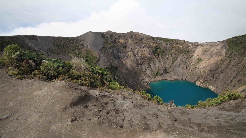 A crater lake surrounded by rugged terrain and sparse vegetation.