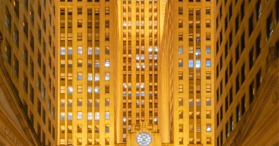 Vista noturna de uma cidade com um edifício iluminado em destaque, com um relógio e colunas.