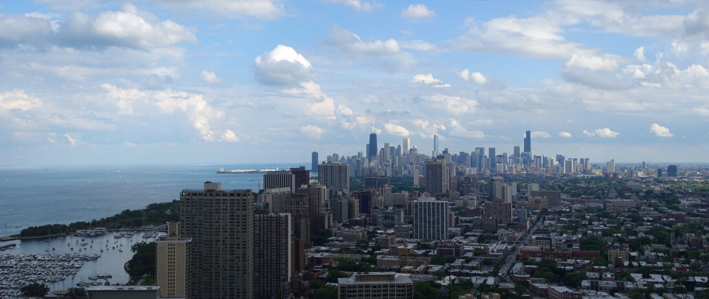 The view of the downtown Chicago skyline under the fluffy white clouds and blue sky as seen from the rooftop deck of the New York condos.