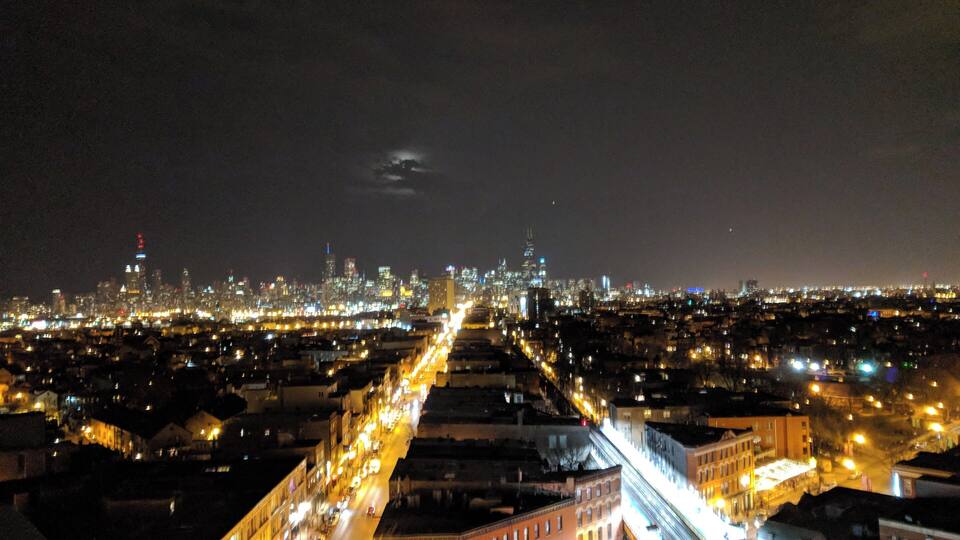 Eine beleuchtete Stadtlandschaft bei Nacht, mit Gebäuden und einem Fluss.