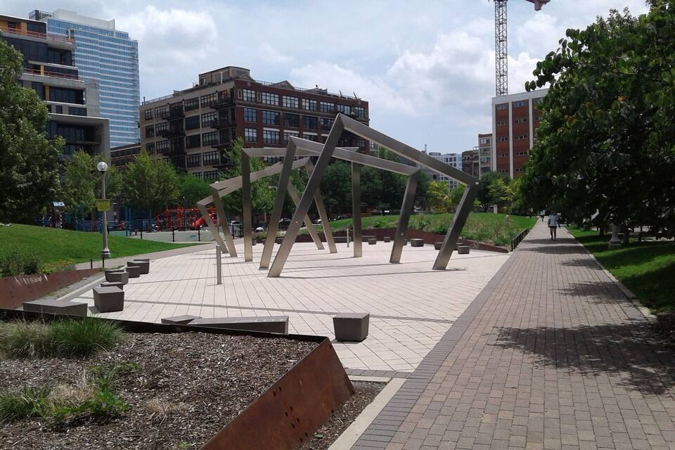 Un parc agrémenté d’une sculpture moderne, de sentiers pavés et entouré de bâtiments.
