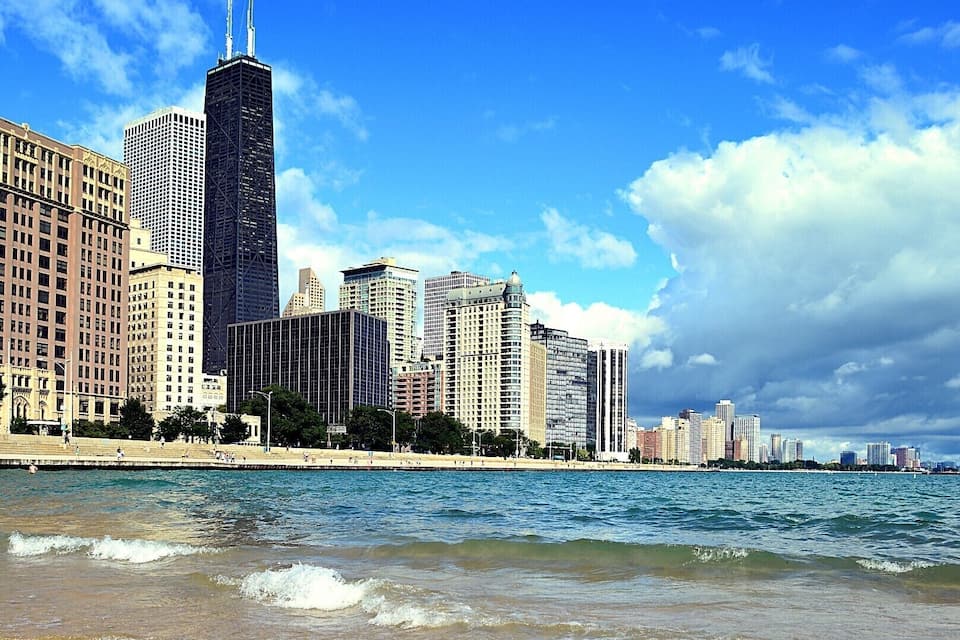 A beach with sand and seaweed, a city skyline with tall buildings, and a clear blue sky with clouds.