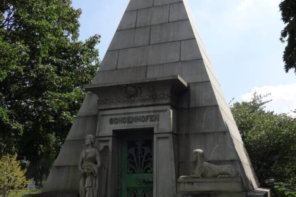 A pyramid-shaped monument with a green door, a statue of a woman, and a lion statue.