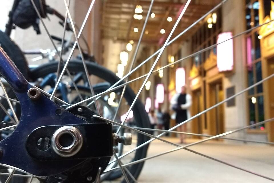 Une roue de vélo avec une chaîne, et en arrière-plan, une enseigne indiquant « OPÉRA-BALLET CIVIQUE ».