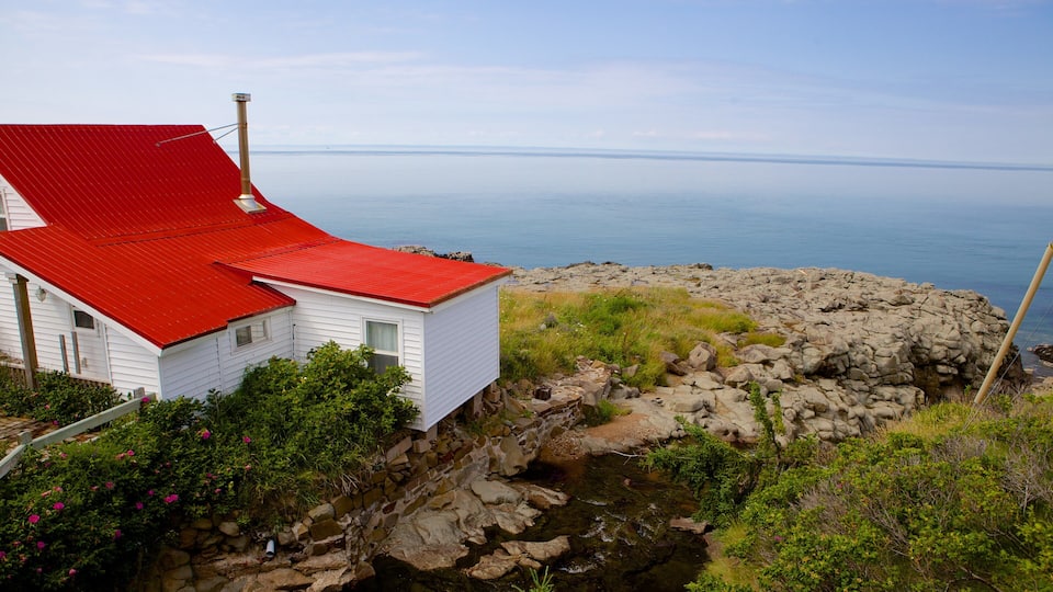 A white house with a red roof by a rocky shoreline with a view of the ocean.