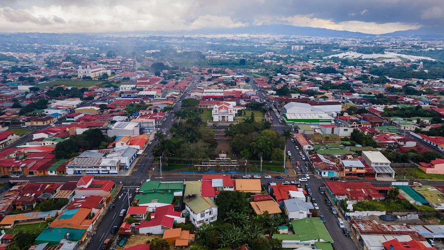 An aerial view of a city with a central plaza, surrounded by colorful buildings and a river in the background.