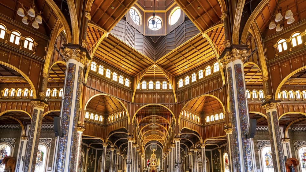 An ornate church interior with high vaulted ceilings, intricate woodwork, and stained glass windows.