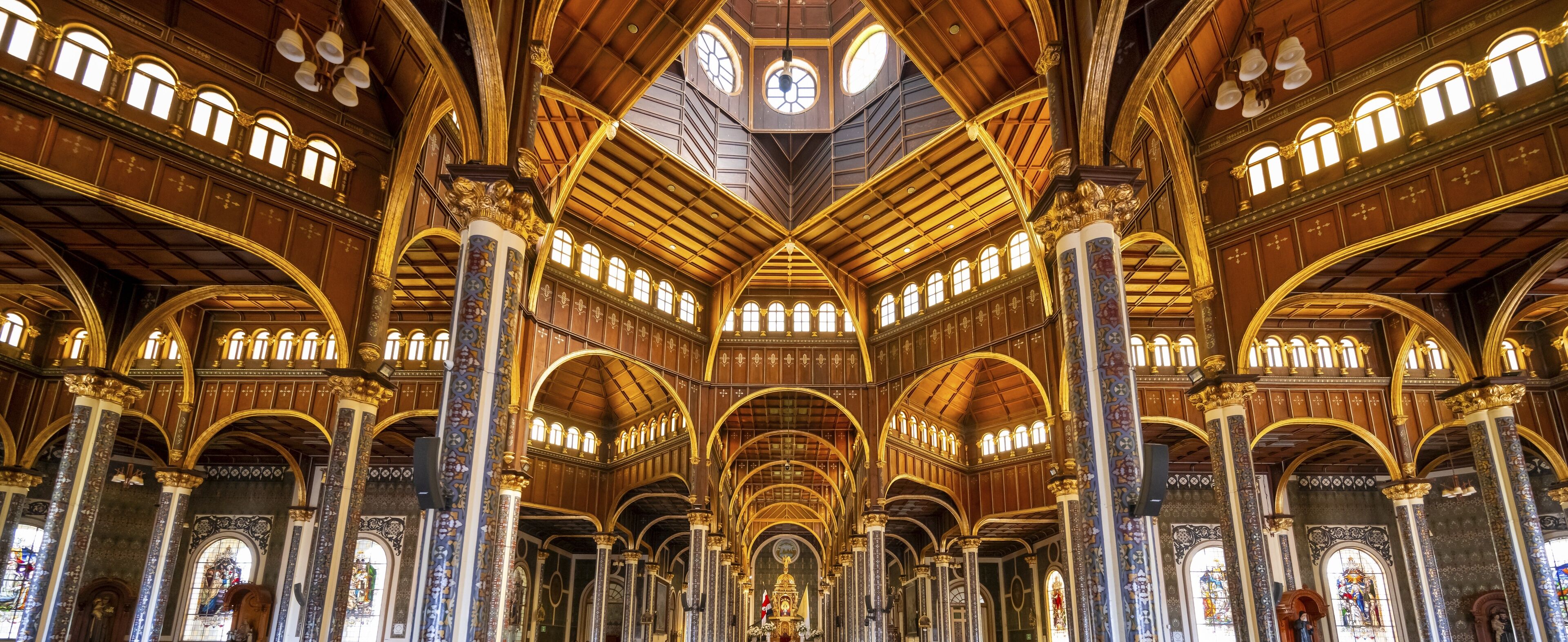 An ornate church interior with high vaulted ceilings, intricate woodwork, and stained glass windows.