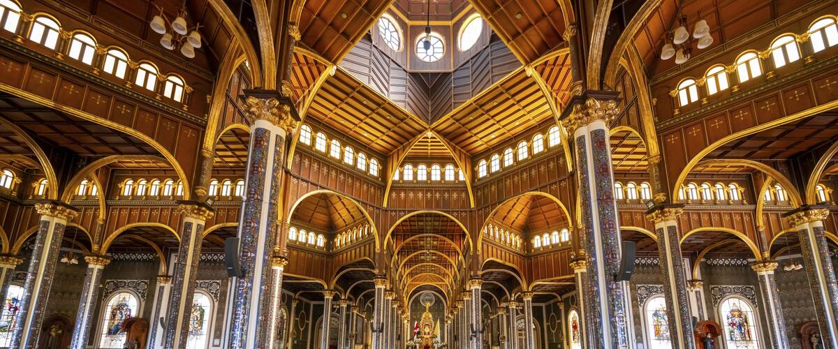 An ornate church interior with high vaulted ceilings, intricate woodwork, and stained glass windows.