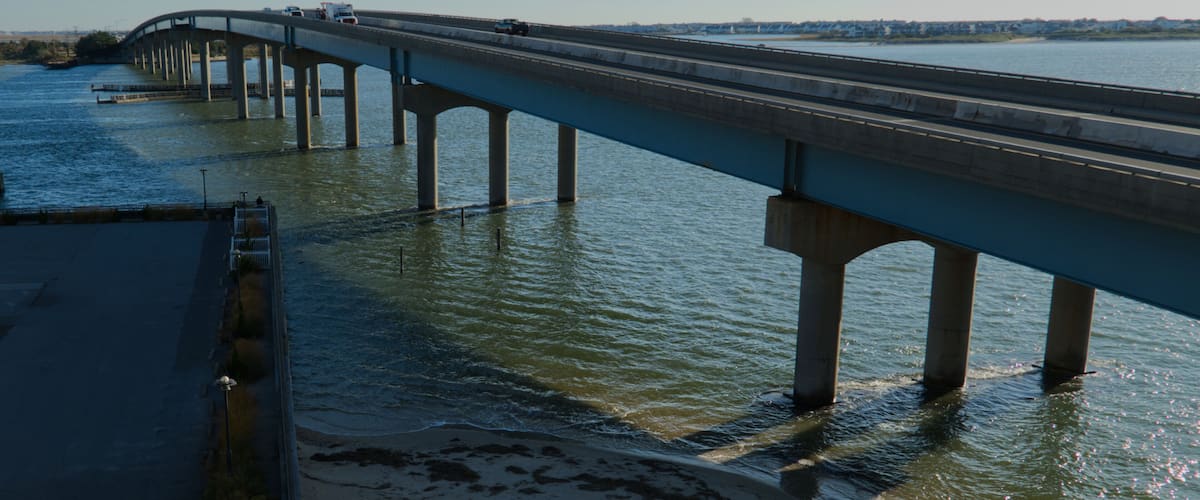 A bridge over a river with multiple piers, a clear sky, and distant buildings.