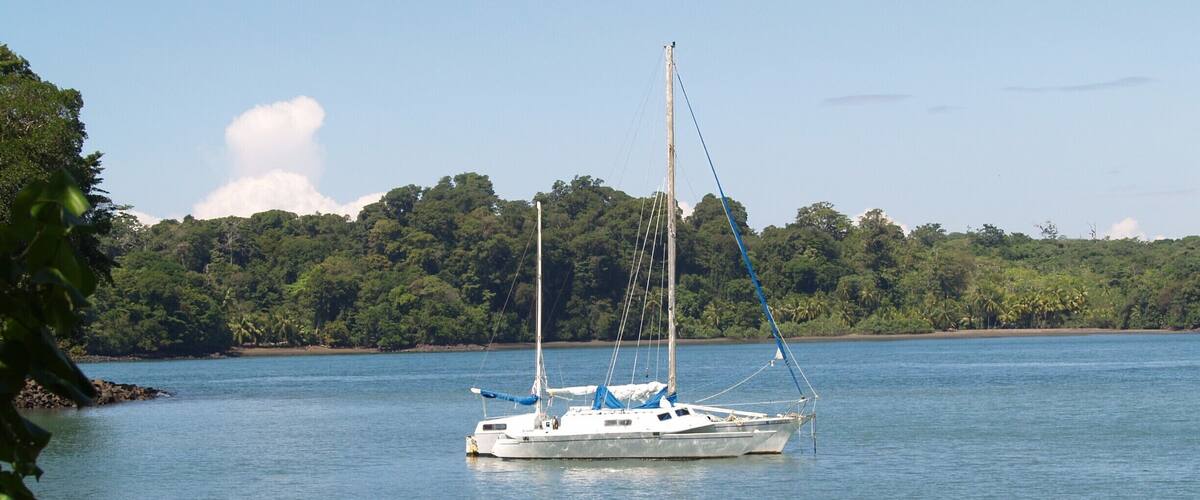 A sailboat on calm waters with a forested shoreline in the background.
