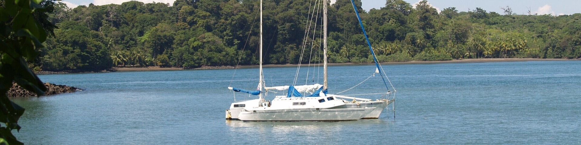 A sailboat on calm waters with a forested shoreline in the background.