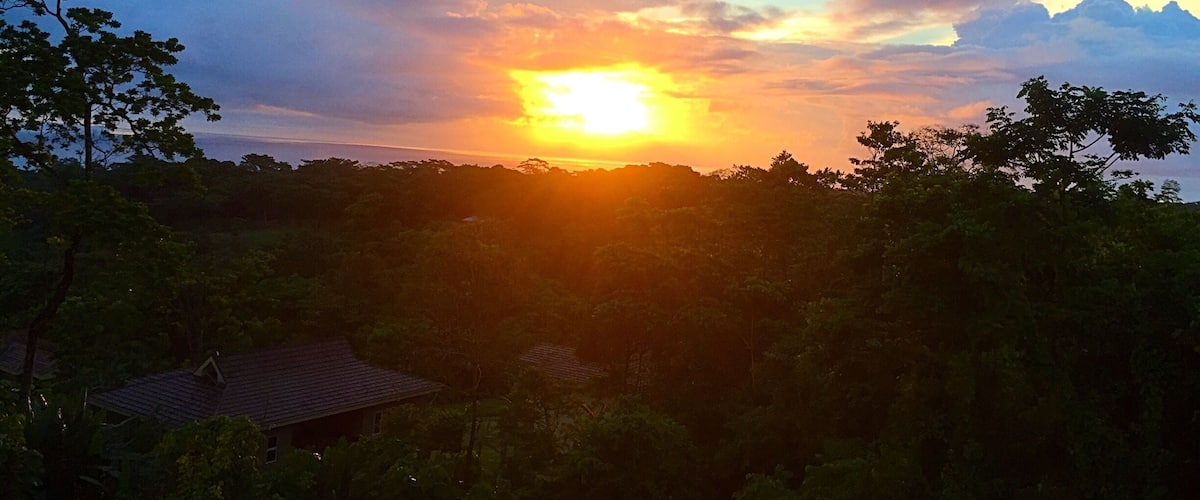 A sunset over a forested landscape with a house in the foreground.