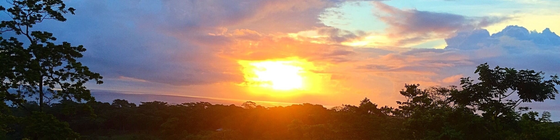 A sunset over a forested landscape with a house in the foreground.