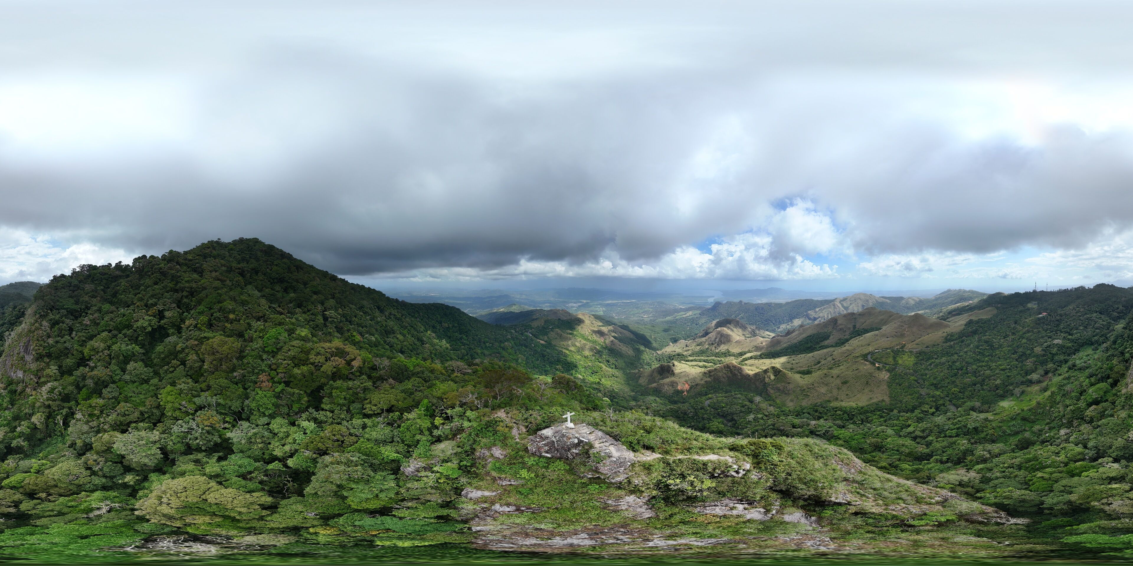 A lush valley with dense green forests, rolling hills, and a cloudy sky.
