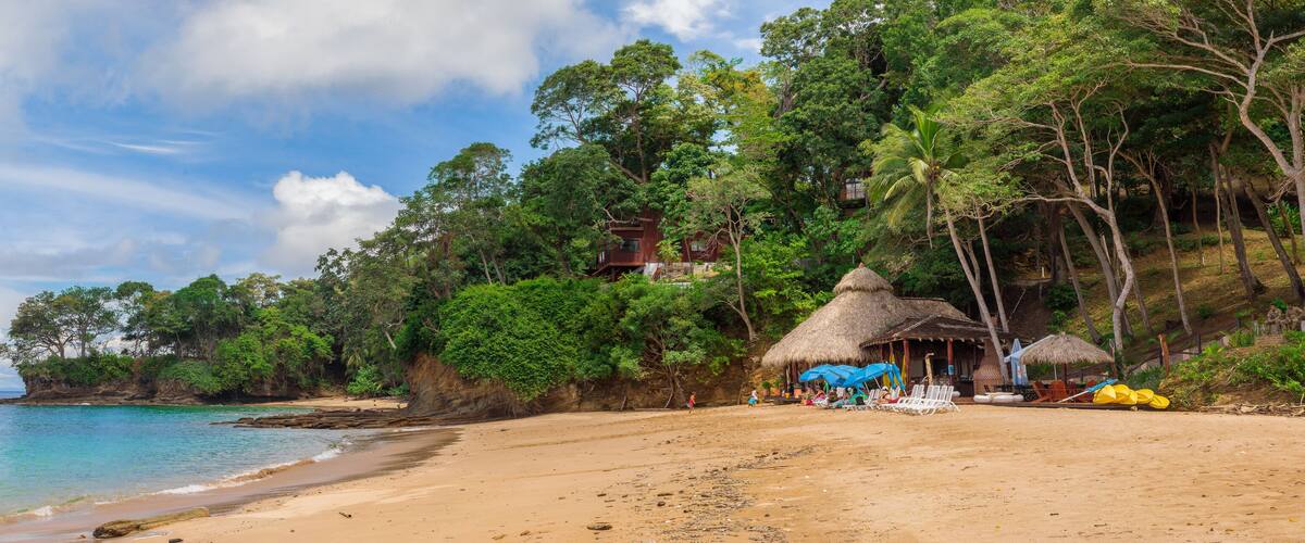 A beach with a thatched-roof hut, a rocky cliff, and lush greenery.