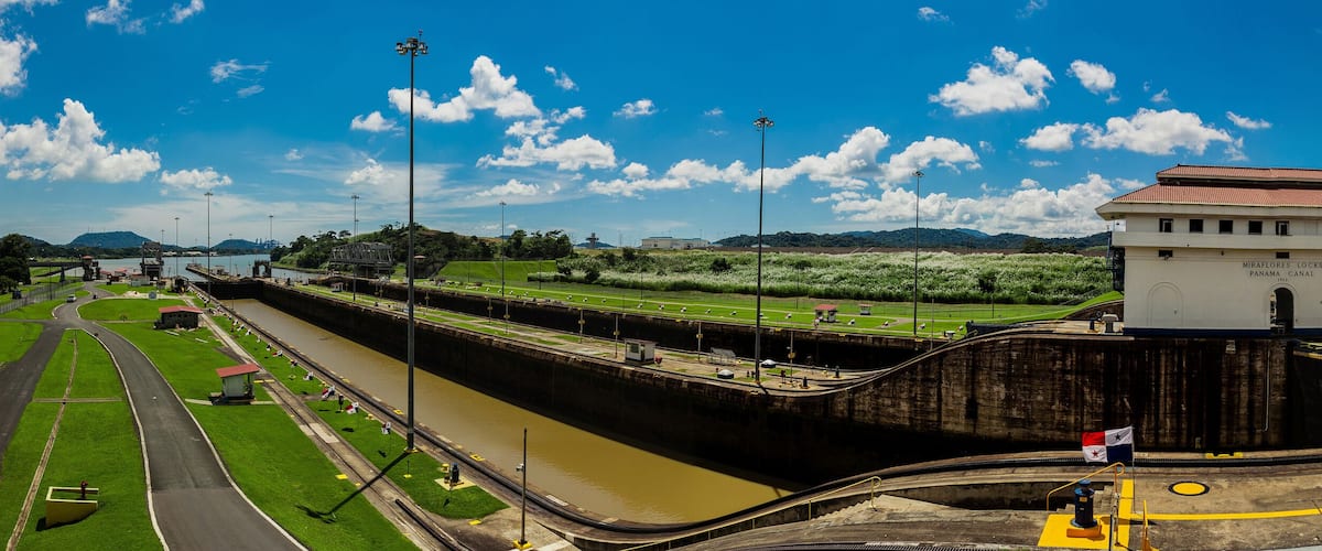 A lock system with a tower labeled "Miraflores Locks Panama Canal" and a green landscape with a road and water.